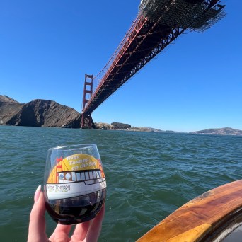 Wine Tasting on the Bay glass with red wine held up under the Golden Gate Bridge, San Francisco Bay