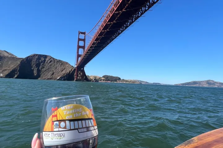 Wine Tasting on the Bay glass with red wine held up under the Golden Gate Bridge, San Francisco Bay