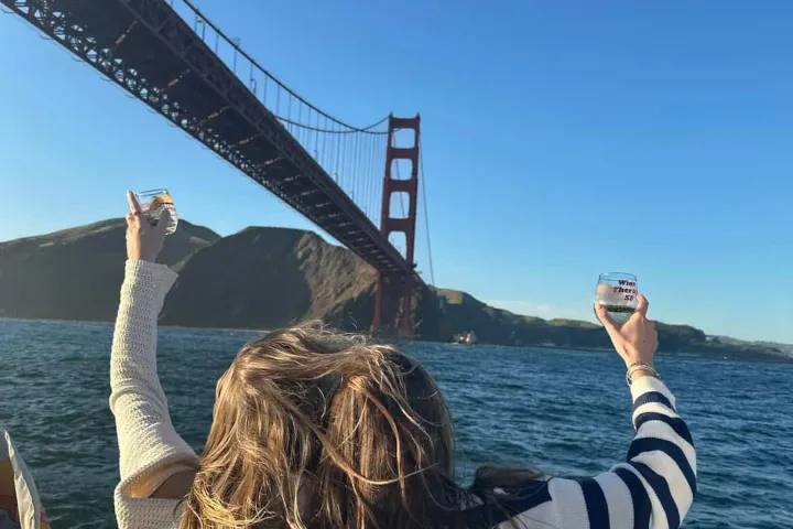 Guests raising Wine Therapy SF glasses toward the Golden Gate Bridge on San Francisco Bay cruise